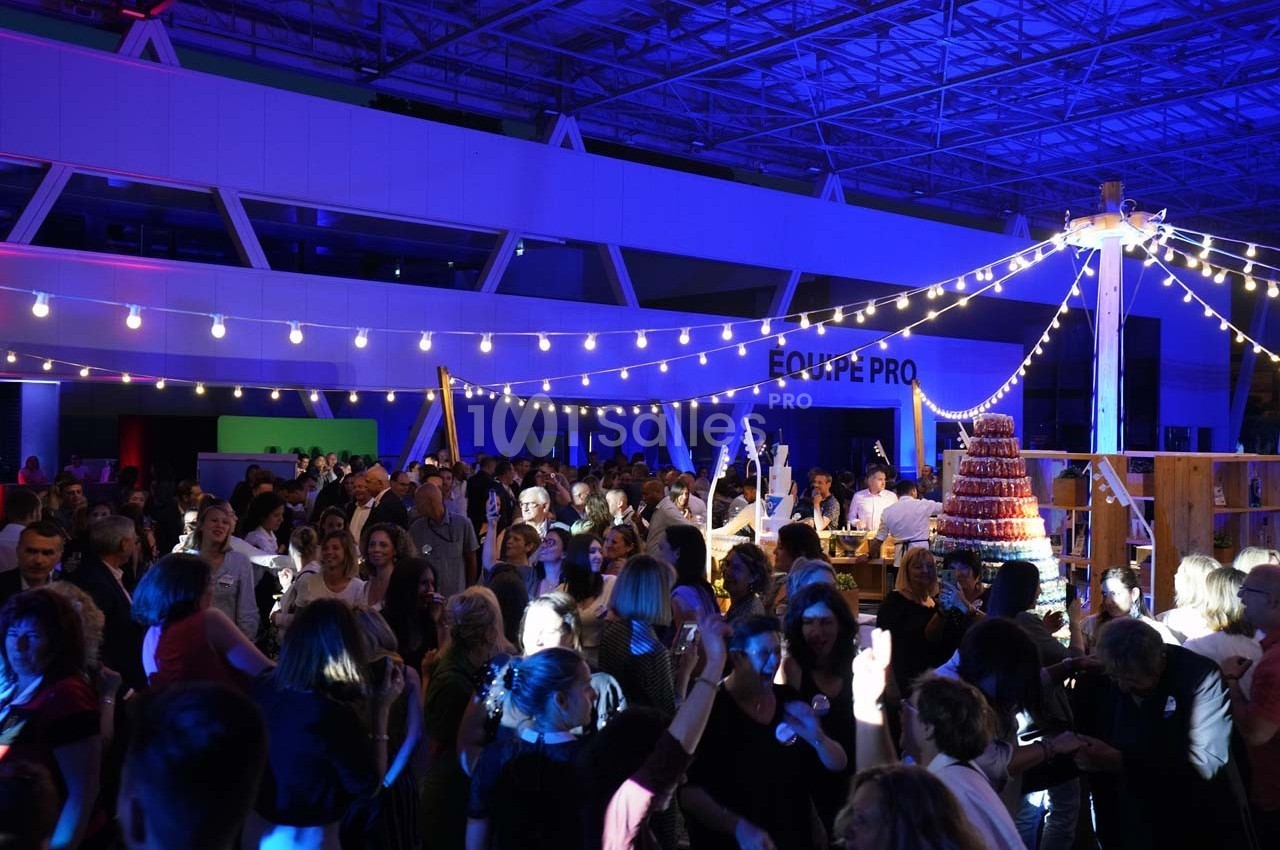 Foule dans un espace intérieur décoré de guirlandes lumineuses, participant à un événement festif en soirée.