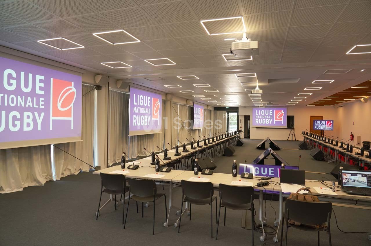 Salle de conférence équipée de tables, chaises, micros et écrans affichant ’Ligue Nationale Rugby’.