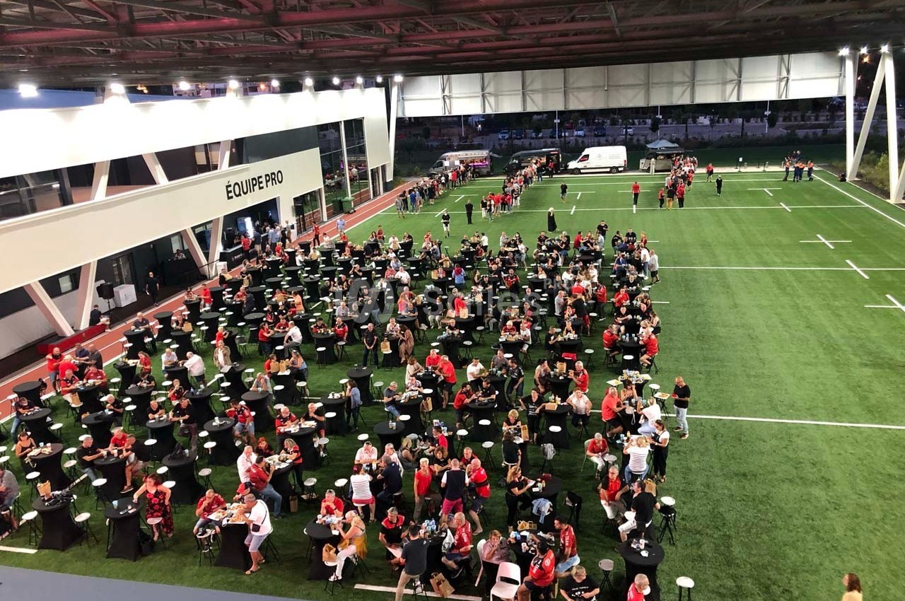 Des personnes assises et debout participent à un événement convivial sur un terrain de sport couvert.