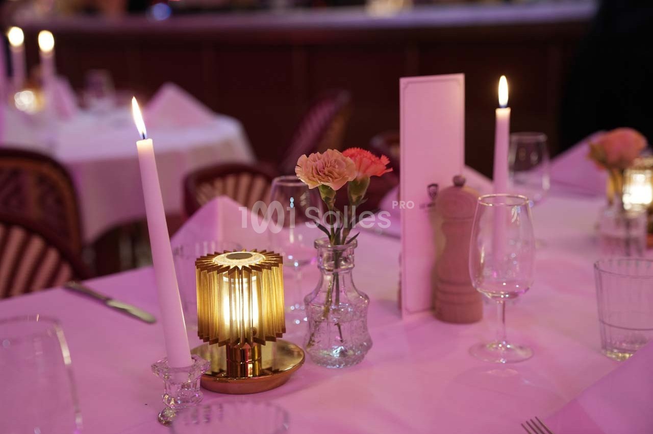 Table dressée avec bougies allumées, fleurs dans un vase, verres et accessoires de table dans une ambiance tamisée.