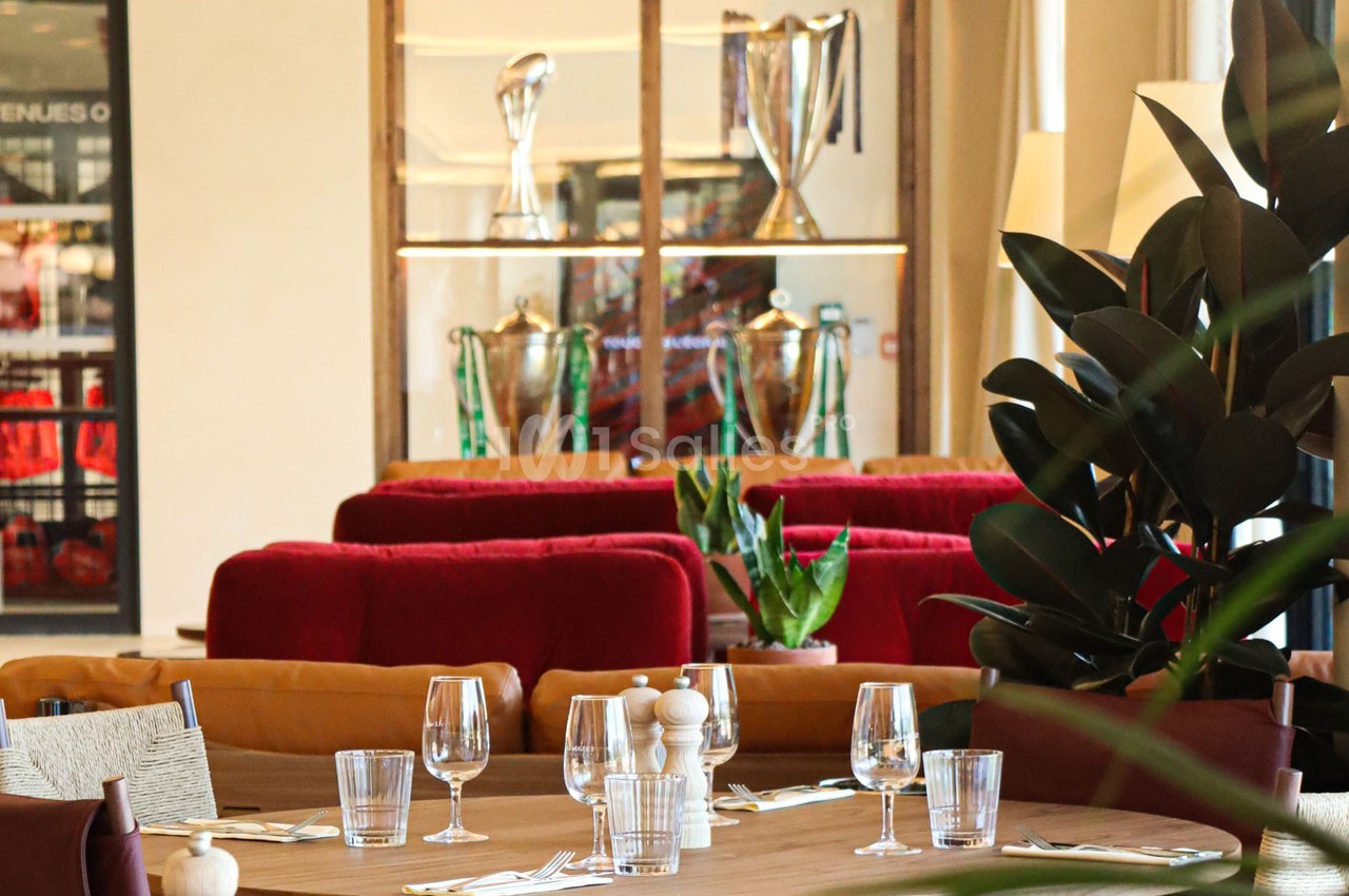 Salle de restaurant élégante avec tables dressées, plantes et vitrines exposant des trophées en arrière-plan.