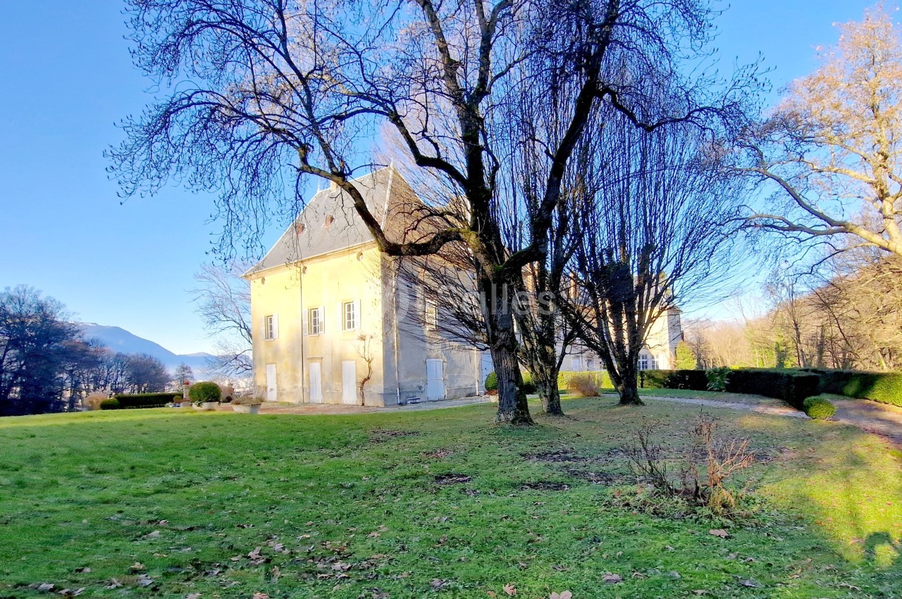 Manoir ancien entouré d'arbres dénudés en hiver, situé dans un parc verdoyant sous un ciel bleu clair.