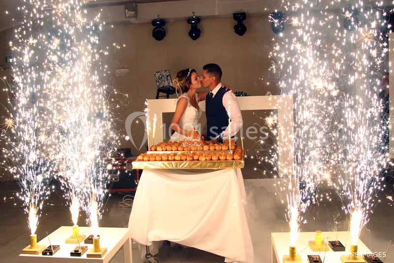 Un couple de mariés s'embrasse devant une pièce montée entourée de fontaines lumineuses en intérieur.