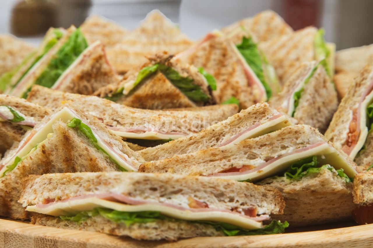 Assortiment de sandwichs triangulaires garnis de jambon, fromage, laitue et tomate sur un plateau en bois.