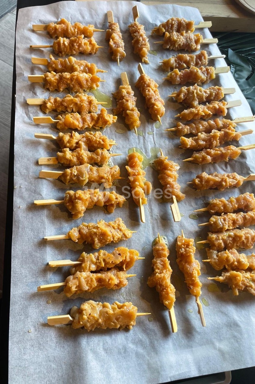 Brochettes de viande marinée alignées sur une plaque recouverte de papier sulfurisé, prêtes à être cuites.