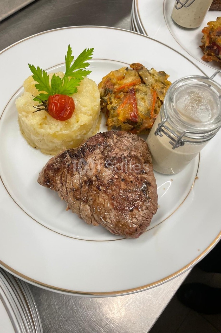 Assiette composée d'un steak grillé, d'une purée garnie, d'un gratin de légumes et d'une sauce en pot individuel.