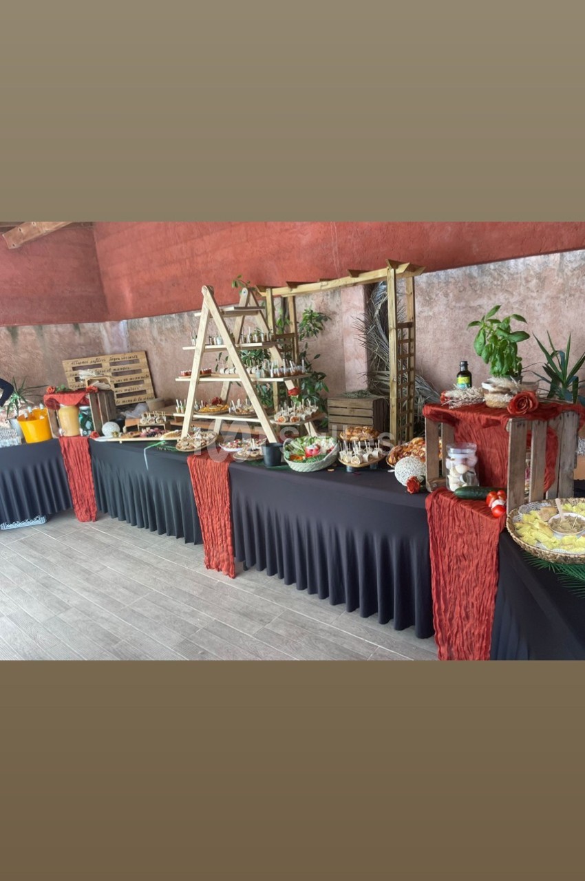 Buffet varié avec plats, boissons et décorations végétales sur des tables drapées de noir dans un espace intérieur.