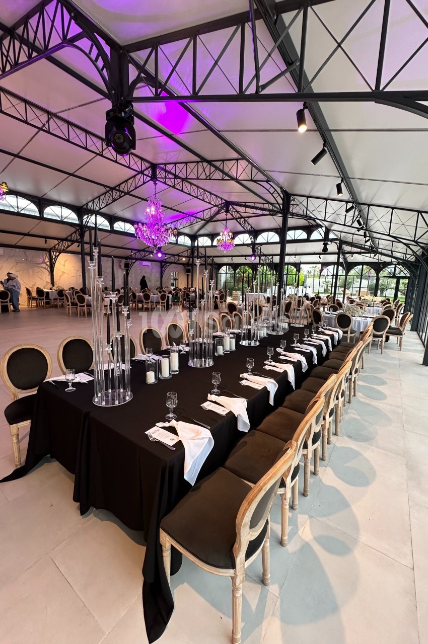Grande table rectangulaire dressée avec une nappe noire, des chandeliers et des chaises élégantes dans une salle lumineuse.