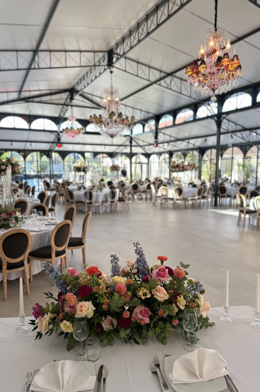 Salle de réception élégante avec tables dressées, chandeliers suspendus et décoration florale colorée au premier plan.