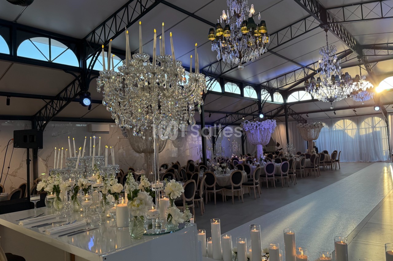 Salle de réception élégante avec chandeliers, bougies et tables décorées pour un événement festif.