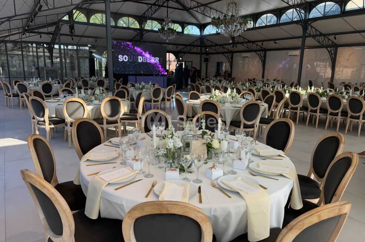 Salle de réception élégante avec tables rondes dressées, décor floral et écran lumineux en arrière-plan.