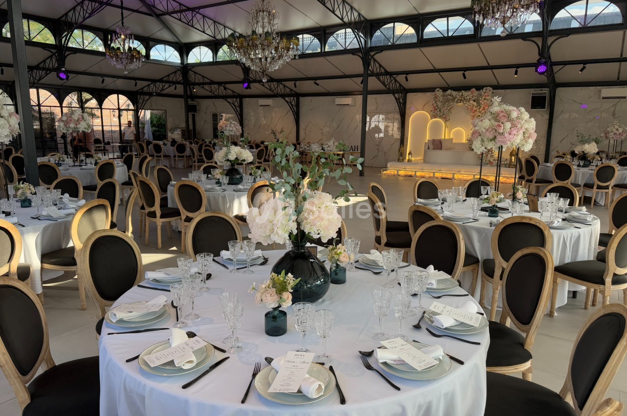 Salle de réception élégante avec tables rondes dressées, décor floral et éclairage chaleureux.