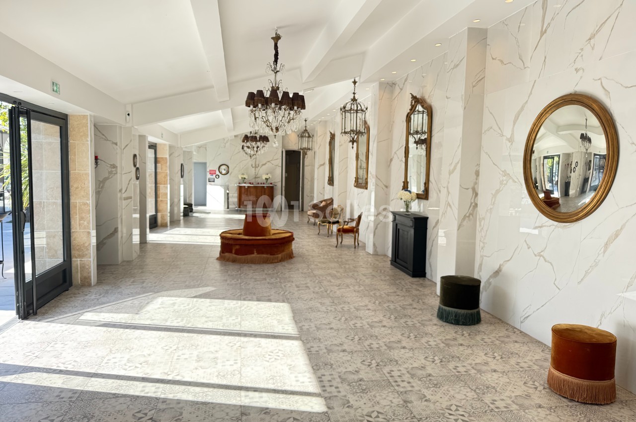 Hall lumineux avec sol en carrelage clair, murs en marbre, miroirs dorés, lustres et mobilier élégant.