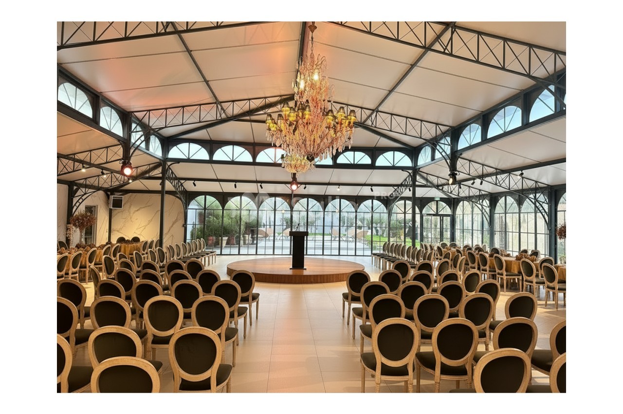 Salle de réception lumineuse avec des rangées de chaises disposées face à une estrade et un pupitre sous un grand lustre.