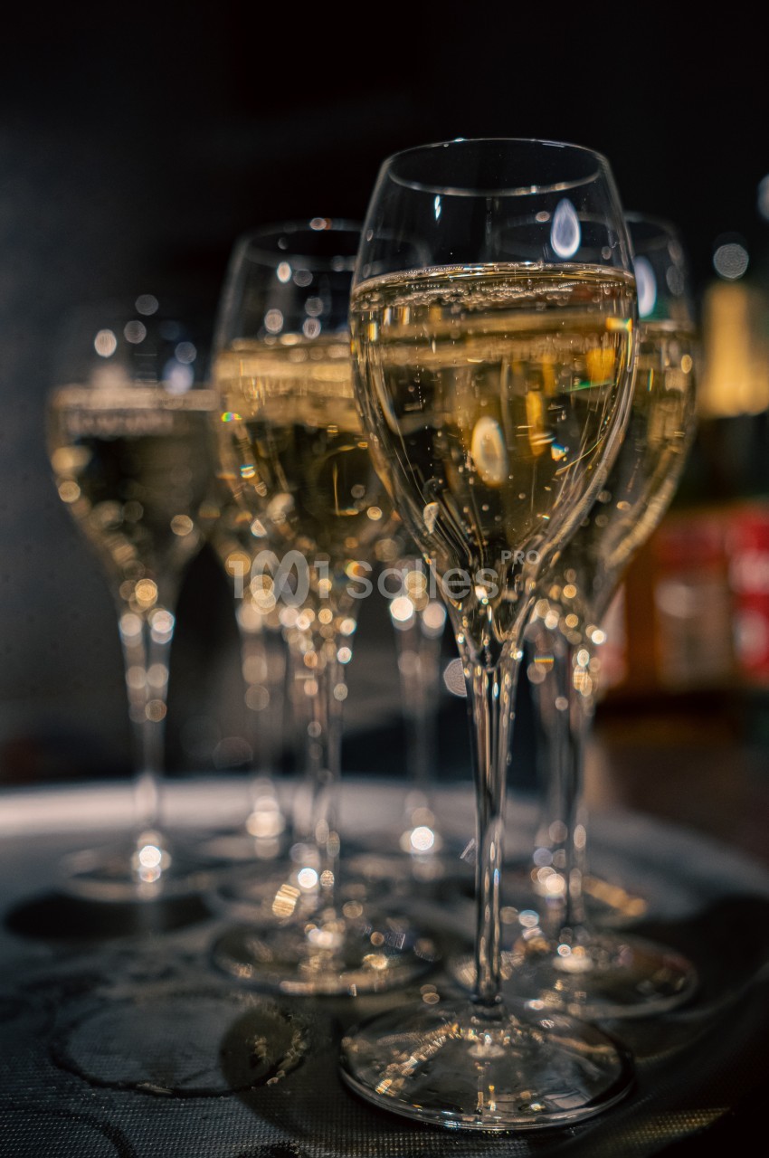 Six flûtes de champagne alignées sur un plateau dans un environnement faiblement éclairé.