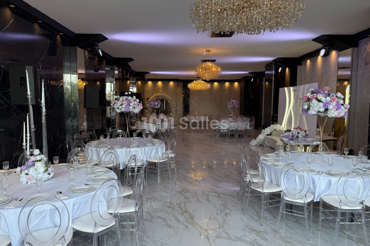 Salle de réception élégante avec tables dressées, chaises transparentes et lustres en cristal.