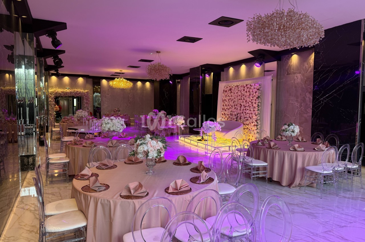Salle de réception élégante avec tables décorées de nappes roses, chaises transparentes et éclairage violet tamisé.