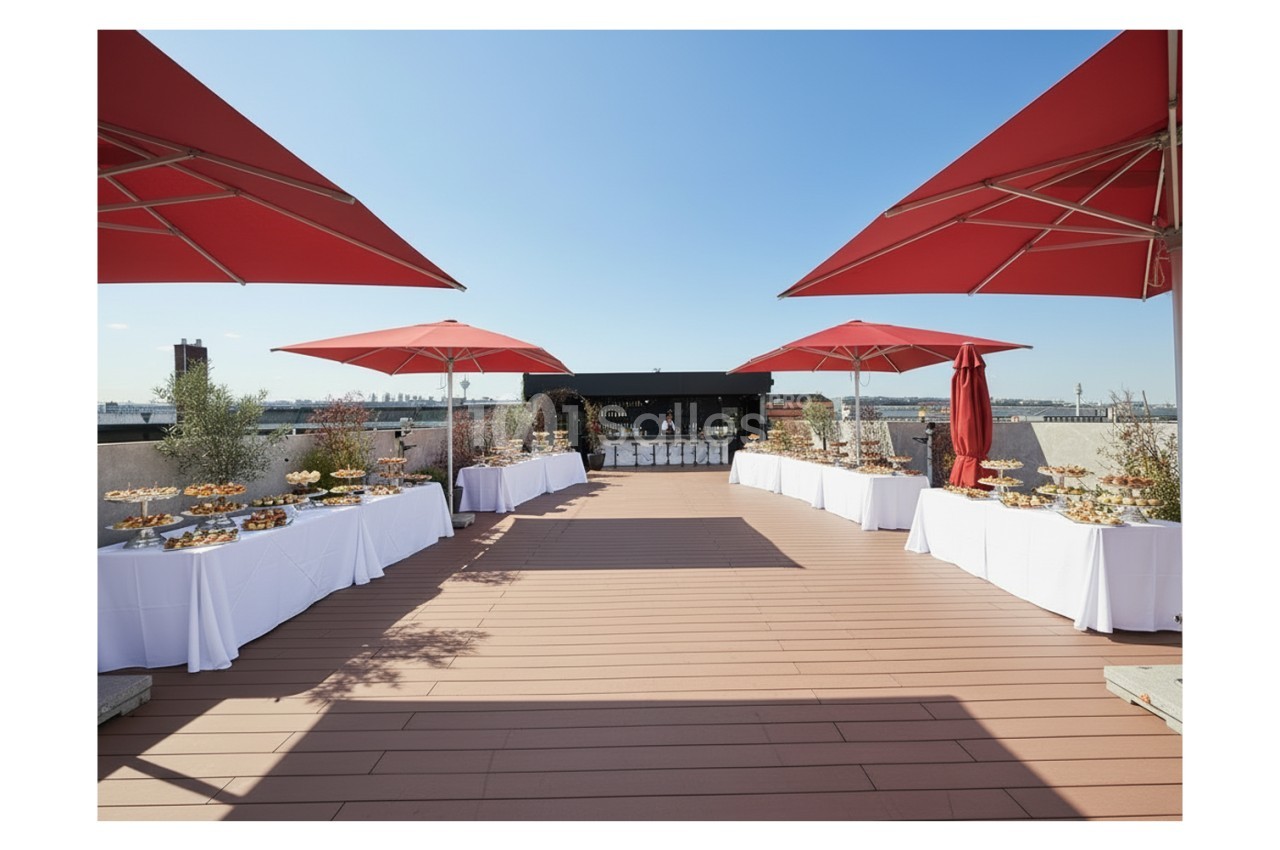 Terrasse ensoleillée aménagée pour un événement, avec tables dressées et parasols rouges.