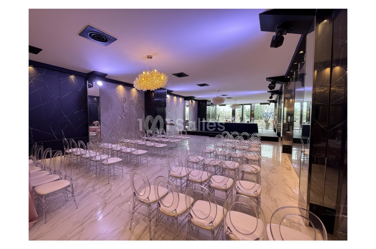 Salle de réception moderne avec chaises transparentes, sol en marbre, murs sombres et éclairage tamisé.