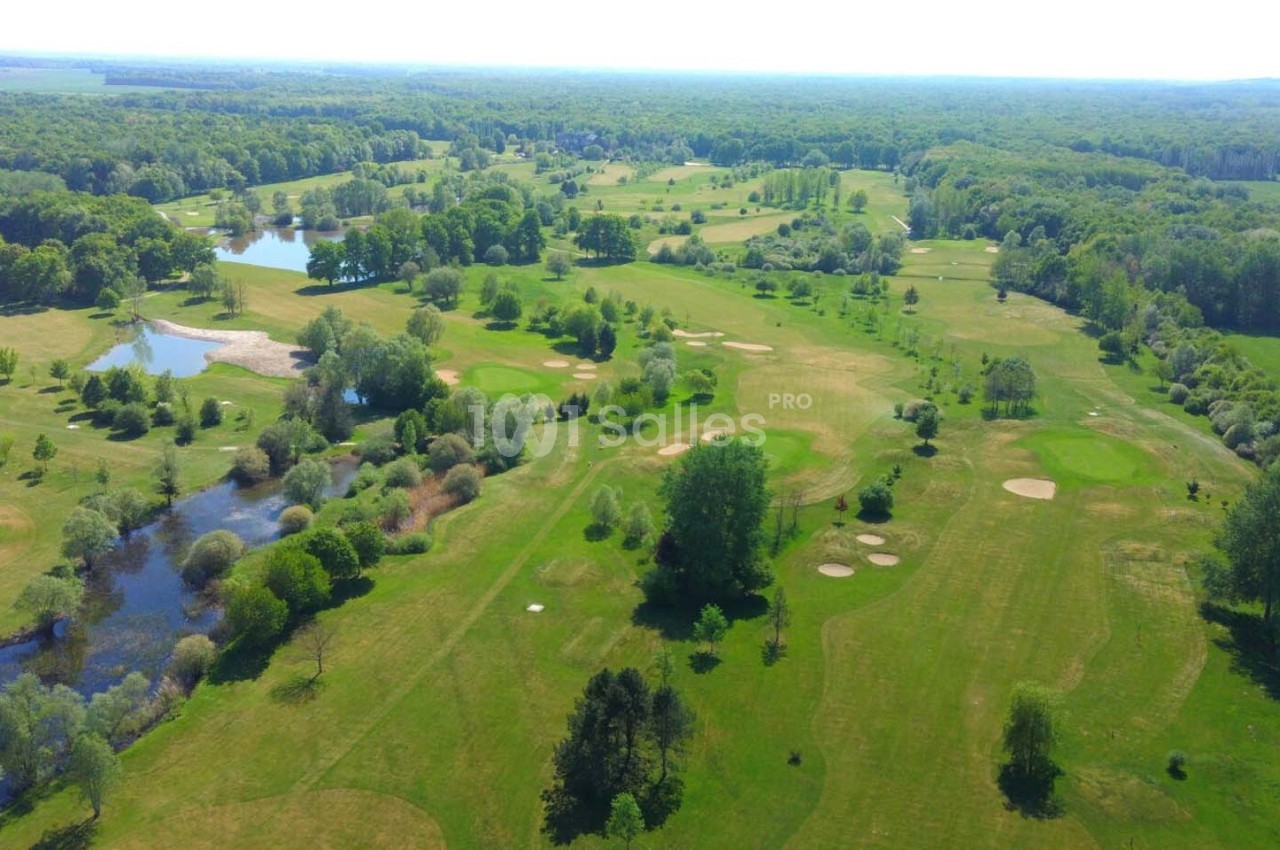Vue aérienne d'un vaste terrain de golf entouré de forêts, avec des étangs et des espaces verts bien entretenus.