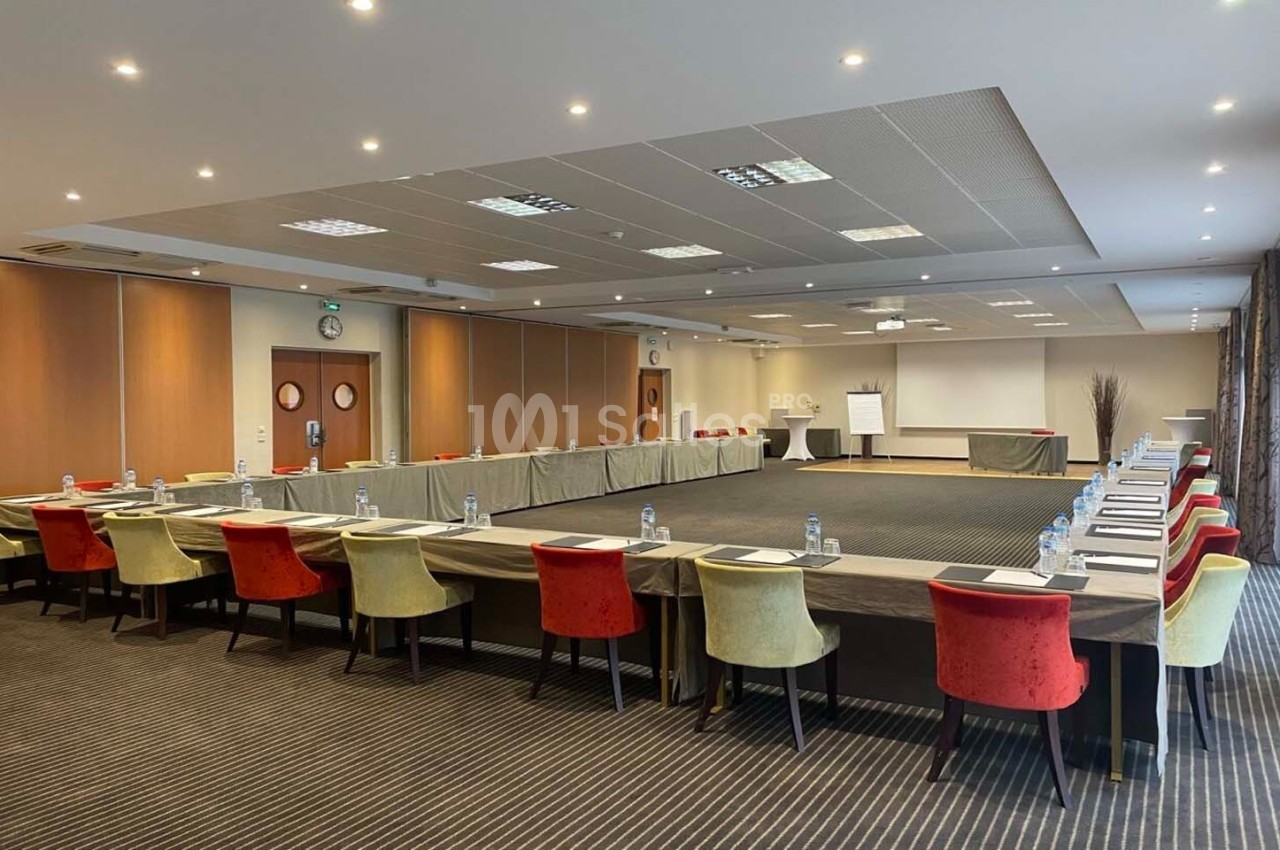 Salle de réunion spacieuse avec tables disposées en U, chaises colorées et équipement de présentation.