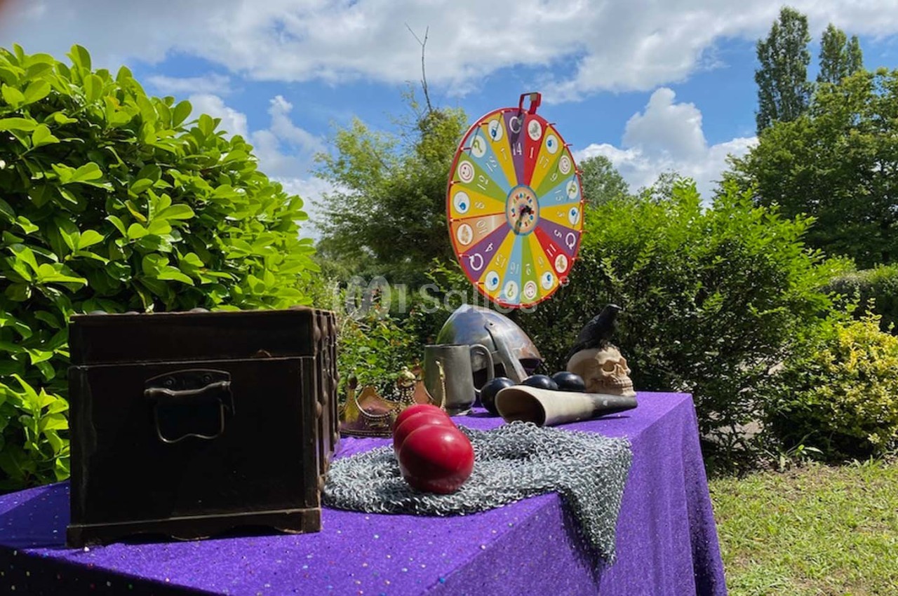 Table avec objets variés, roue colorée en arrière-plan, disposée dans un jardin verdoyant sous un ciel partiellement nuageux.