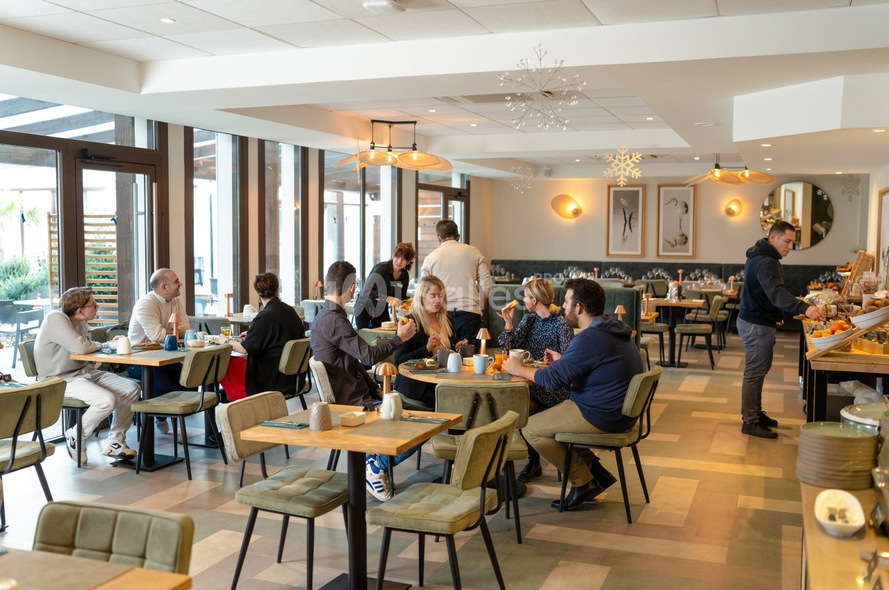 Salle de restaurant lumineuse avec des clients attablés, discutant et prenant leur repas dans une ambiance conviviale.
