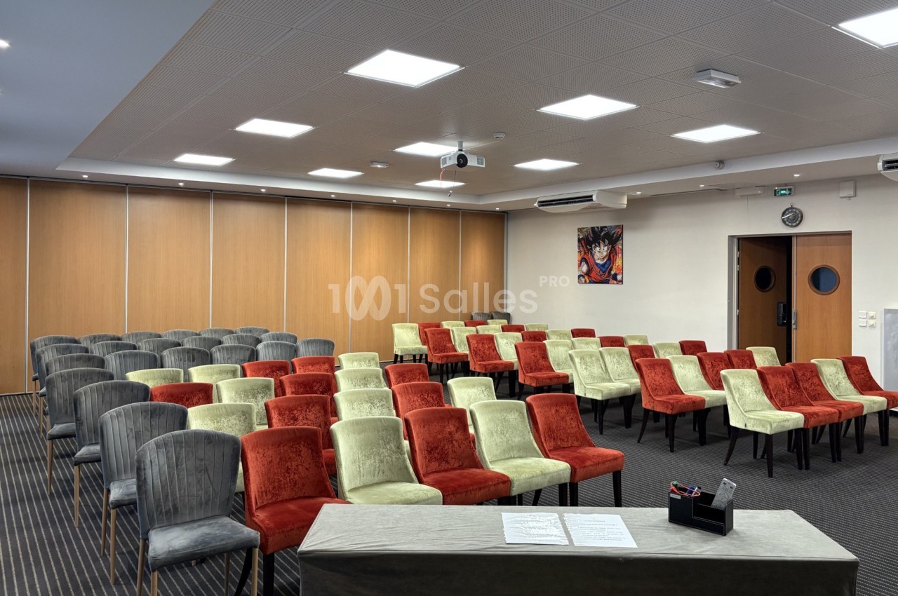 Salle de conférence avec rangées de chaises colorées, un pupitre à l'avant et des panneaux en bois en arrière-plan.