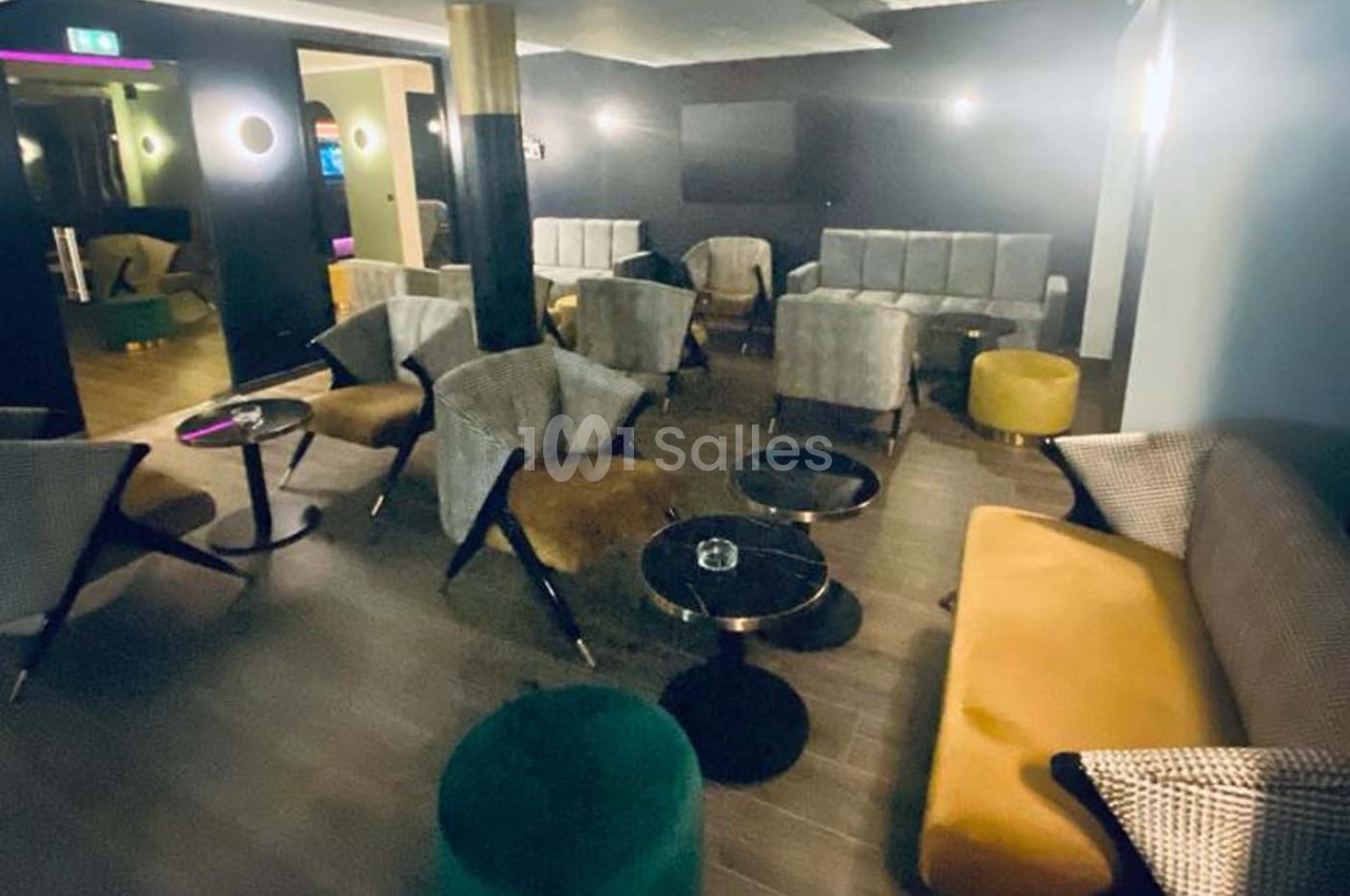 Salon moderne avec fauteuils, canapés, tables basses et éclairage tamisé dans une ambiance conviviale.