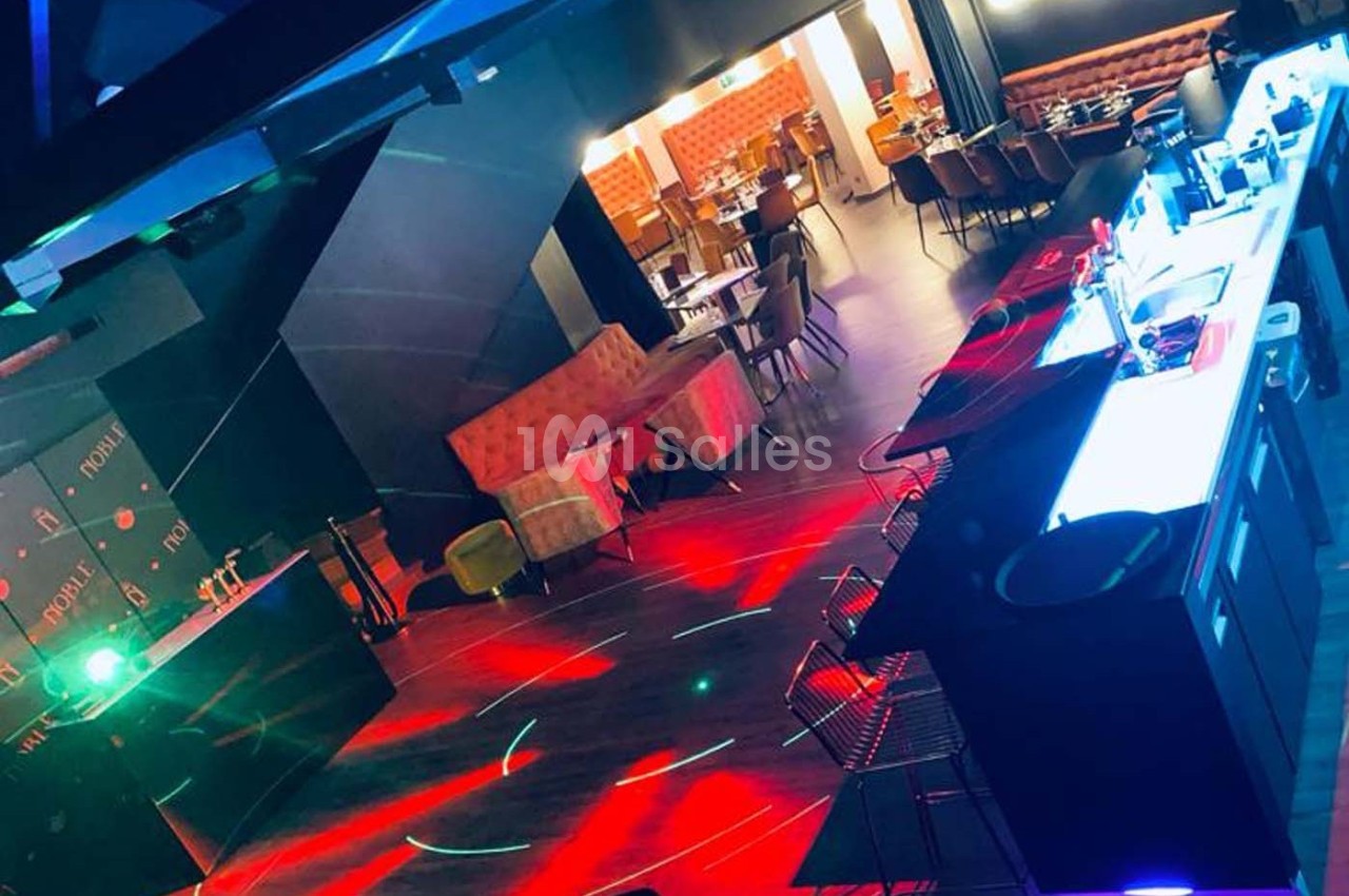 Salle de bar et restaurant avec éclairage coloré, tables dressées et espace ouvert pour des événements.