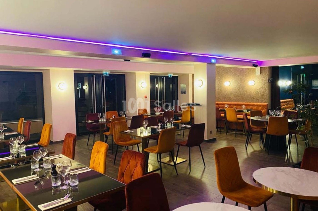 Salle de restaurant moderne avec tables dressées, chaises colorées et éclairage tamisé.