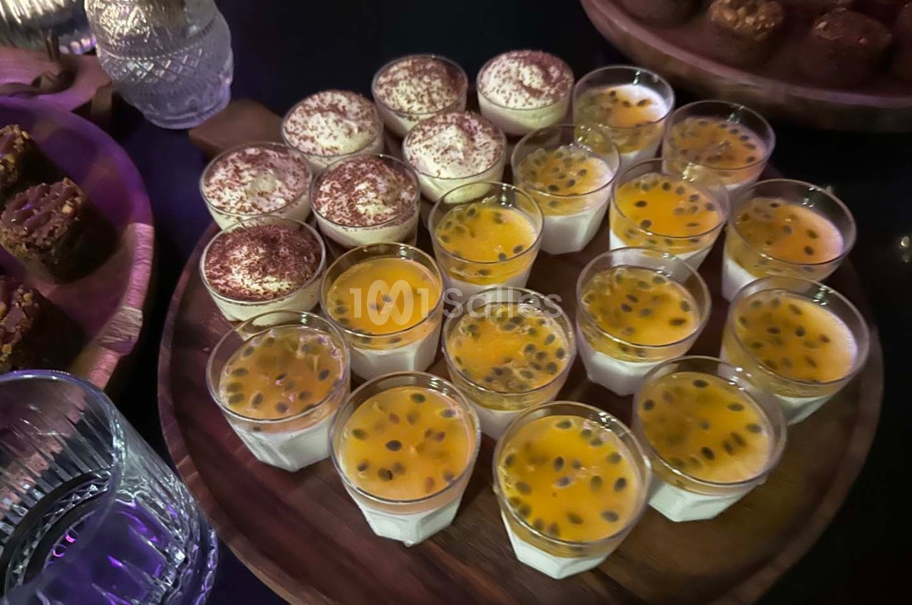 Plateau de verrines avec tiramisus saupoudrés de cacao et desserts au fruit de la passion, entouré de douceurs.