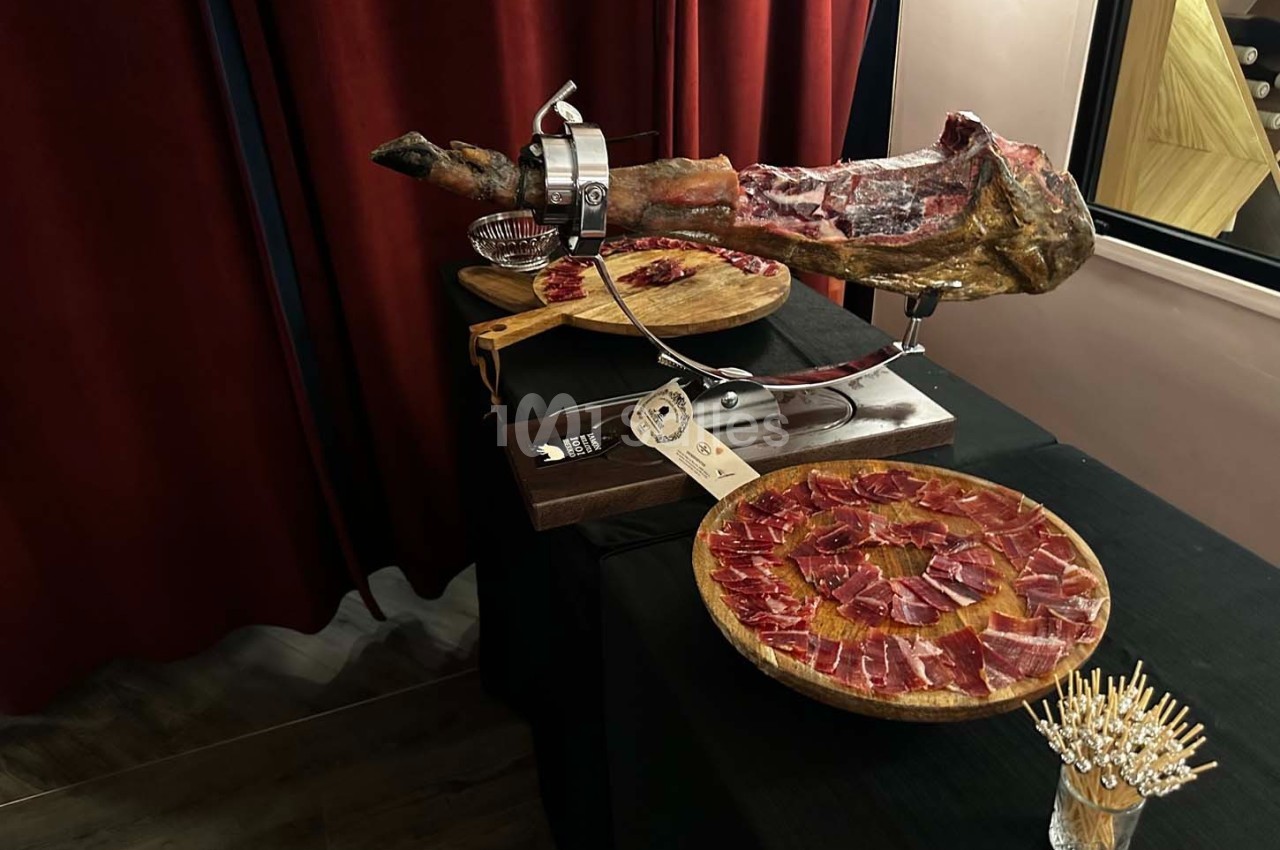 Jambon ibérique sur un support avec des assiettes de tranches fines disposées sur une table noire.