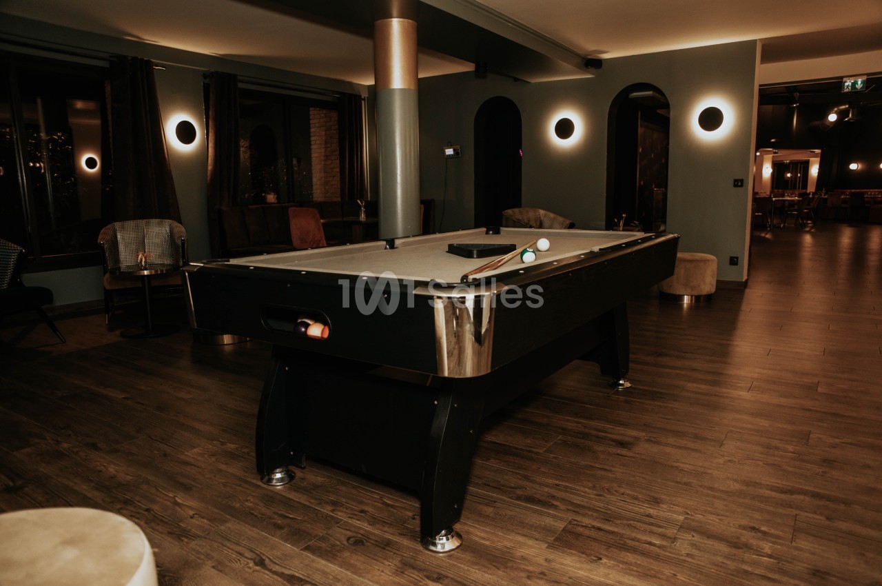 Table de billard noire dans une pièce chaleureuse avec éclairage tamisé et parquet en bois.
