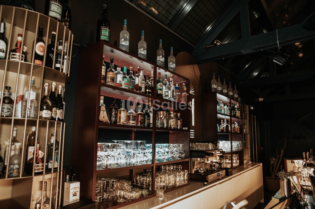Étagères remplies de bouteilles d'alcool et de verres dans un bar à l'ambiance tamisée et moderne.