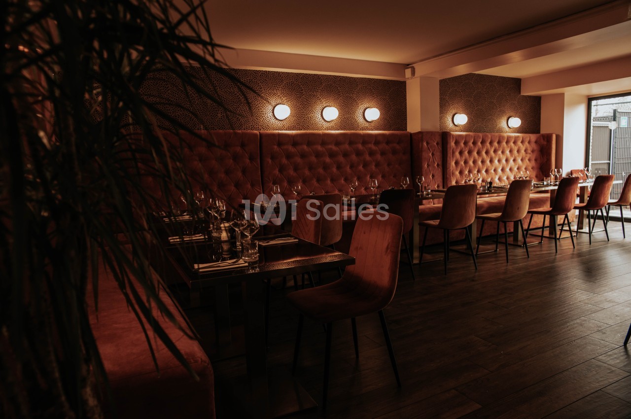 Salle de restaurant chaleureuse avec banquettes capitonnées rouges, chaises en bois et éclairage tamisé.
