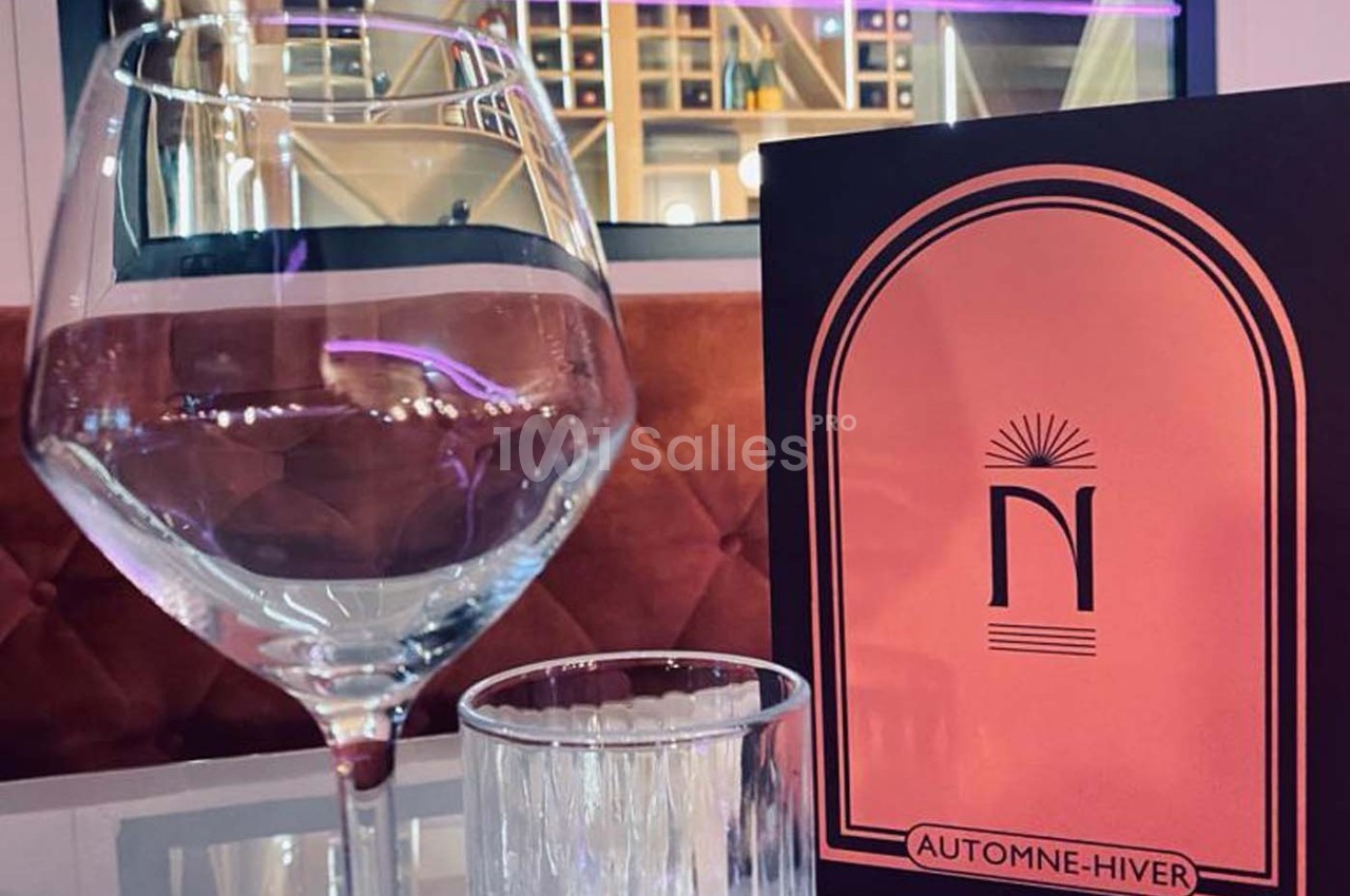 Un verre à vin, un verre d'eau et une carte de menu ’Automne-Hiver’ posés sur une table dans un cadre élégant.
