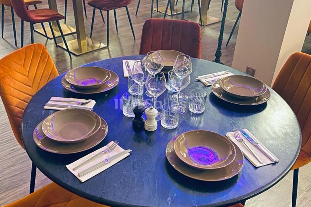Table ronde dressée avec assiettes, verres et couverts, entourée de chaises rembourrées dans un restaurant moderne.