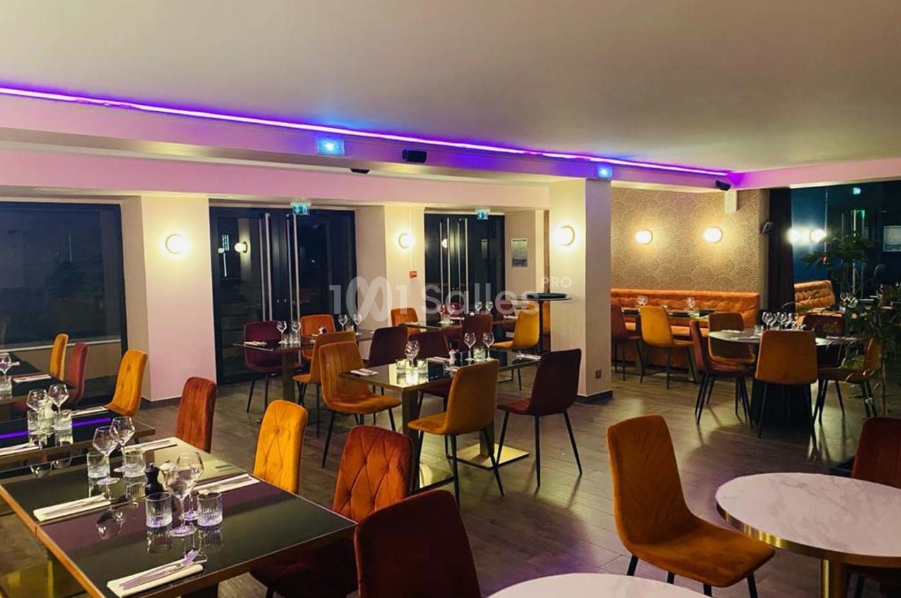 Salle de restaurant moderne avec tables dressées, chaises colorées et éclairage tamisé.