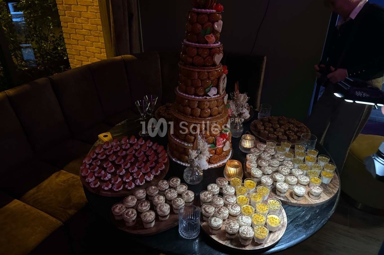 Table garnie de desserts variés, incluant une pièce montée, des verrines et des pâtisseries, dans un cadre tamisé.