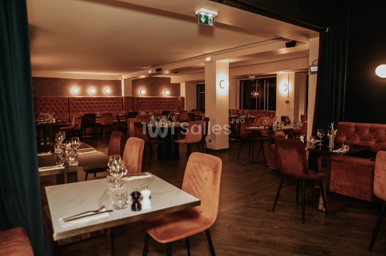 Salle de restaurant élégante avec tables dressées, chaises en velours et éclairage tamisé.