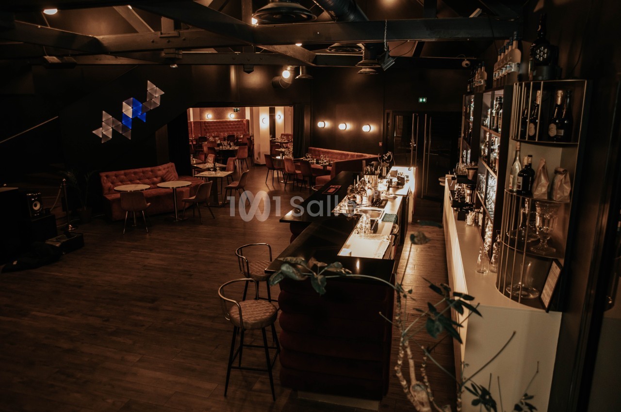 Intérieur d'un bar élégant avec un comptoir éclairé, des tables et des fauteuils dans une ambiance tamisée.