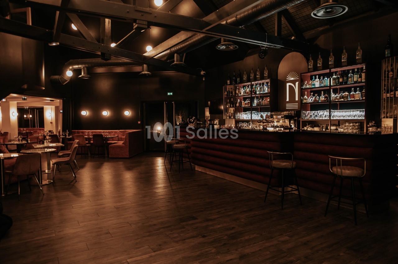 Intérieur d'un bar élégant avec éclairage tamisé, comptoir en bois, étagères de bouteilles et tables disposées autour.