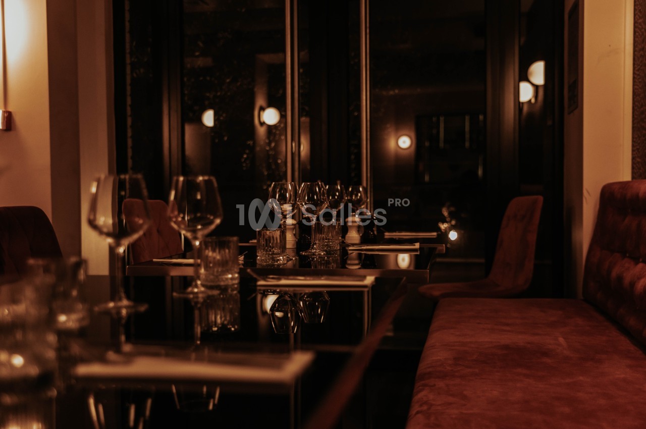 Salle de restaurant élégante avec éclairage tamisé, tables dressées et banquettes en velours rouge.