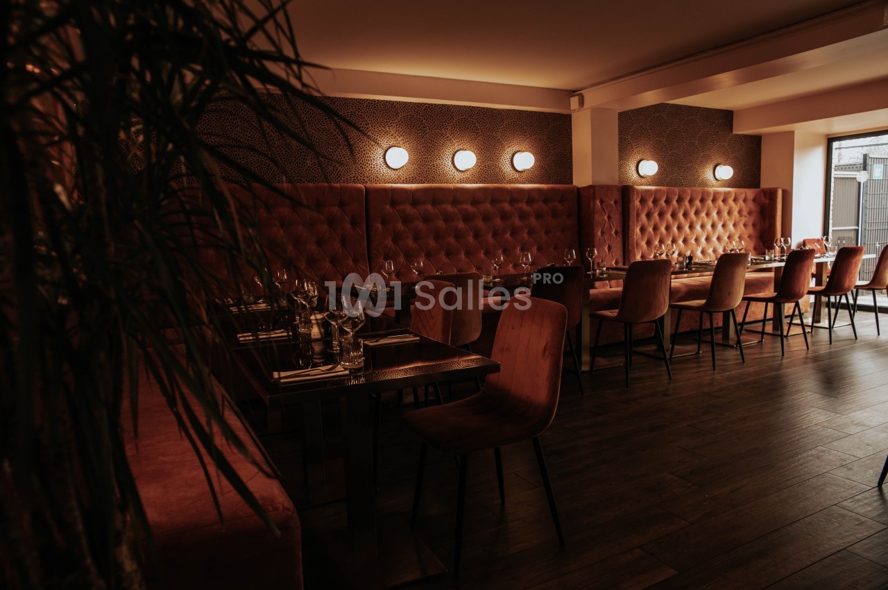 Salle de restaurant chaleureuse avec banquettes en velours rouge, chaises en bois et éclairage tamisé.