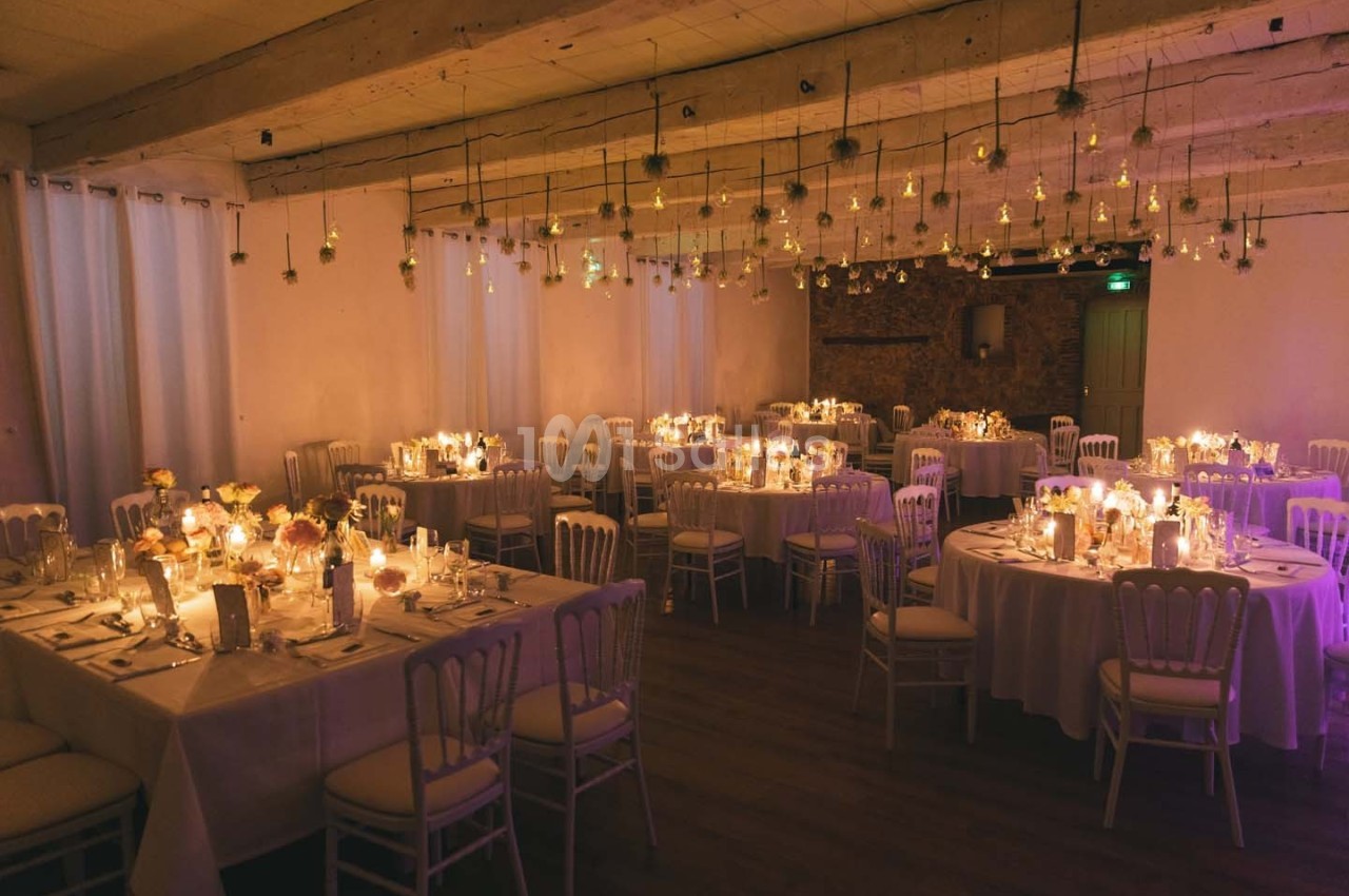 Salle de réception décorée avec des tables rondes, des bougies et des suspensions lumineuses dans une ambiance chaleureuse.