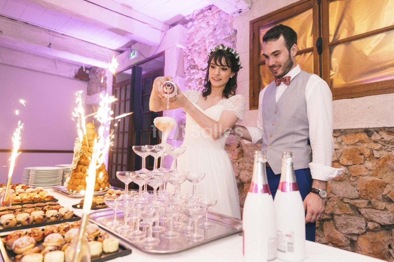 Une mariée verse du champagne dans une pyramide de coupes, accompagnée d'un marié, avec des desserts et des étincelles en…