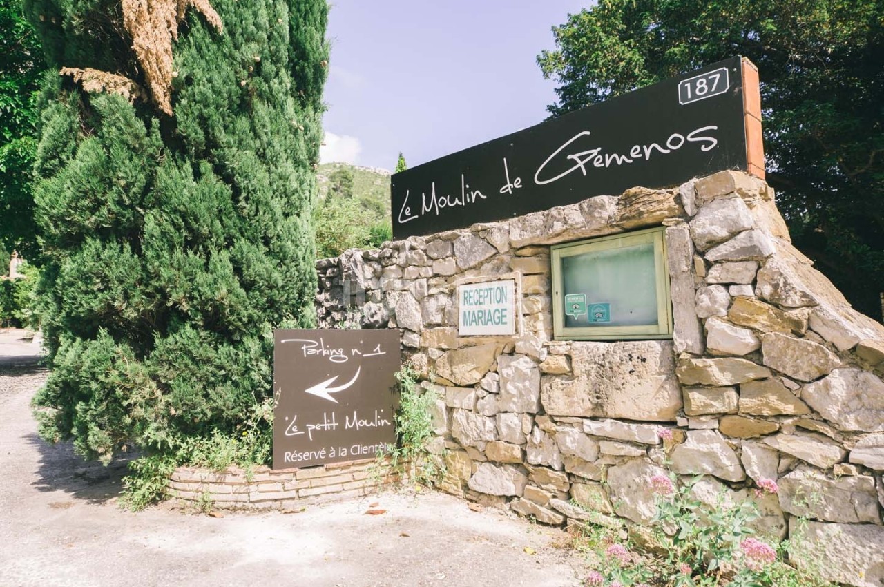 Entrée en pierre avec panneaux indiquant ’Le Moulin de Gémenos’, parking et réception pour mariages.