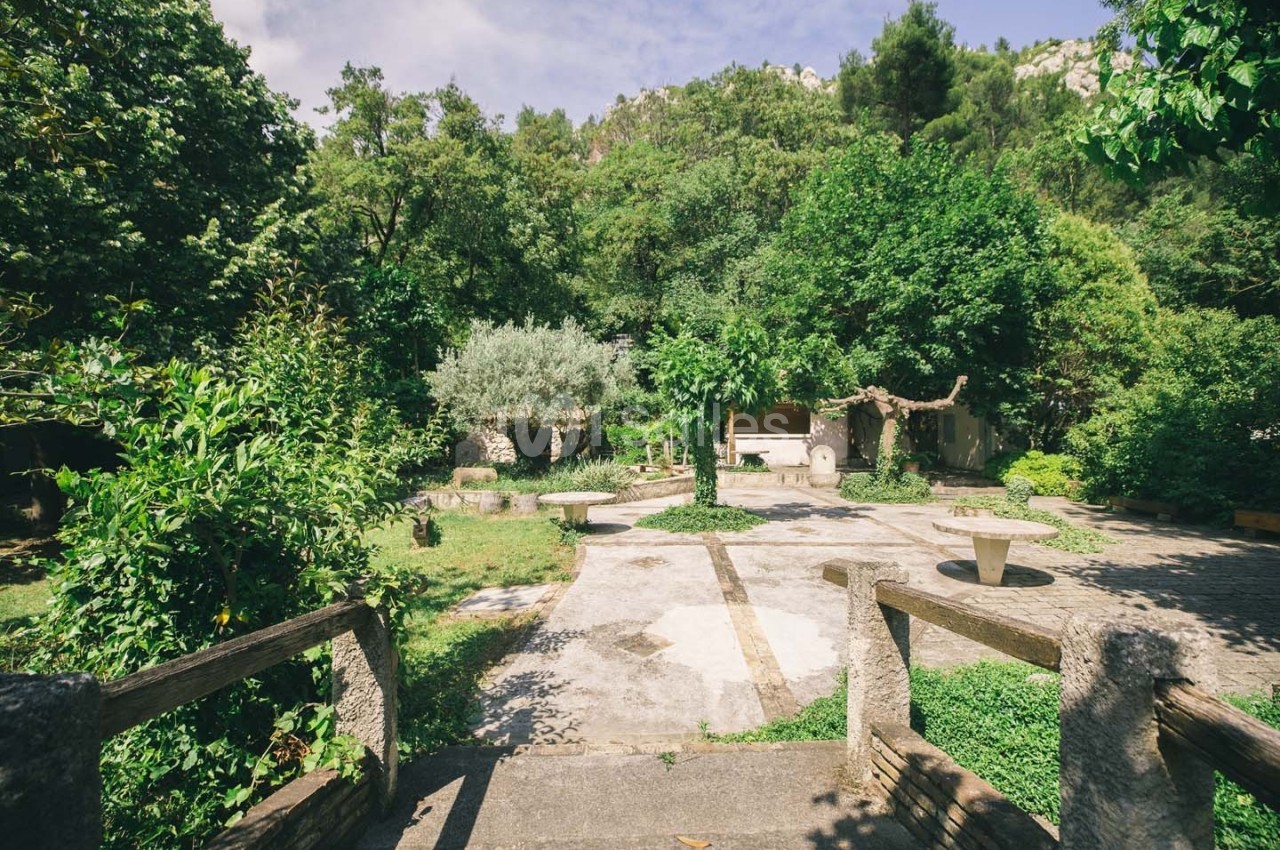 Jardin verdoyant avec des arbres, des tables en pierre et un chemin pavé, vu depuis un escalier en bois.