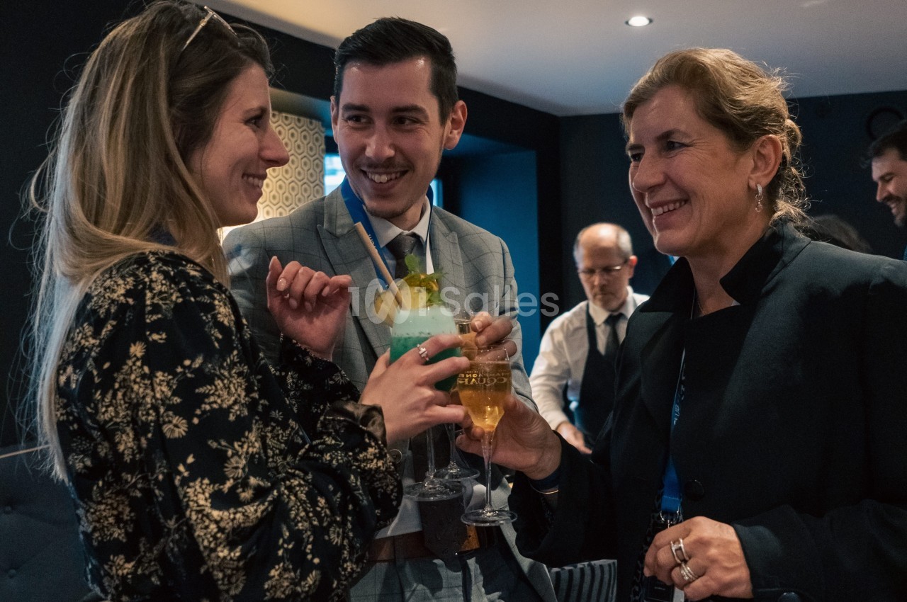 Trois personnes souriantes trinquent avec des verres dans un cadre intérieur convivial.